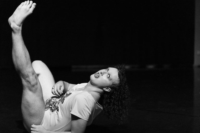 Black and white photo of dancer Alix Kuijpers performing on stage, lying on his back with one leg extended upward in a expressive pose.